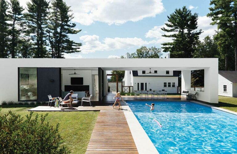 beyaz duvarlı ve siyah detaylı tek katlı ev, bahçede ahşap zeminli havuz
